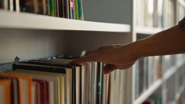 Hand selecting a reference book from a library shelf, representing a lasting traceable research record institutions can cite and build on